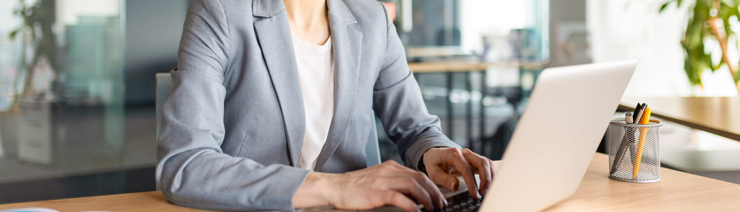 Femme souriante en tailleur gris travaillant sur un ordinateur portable dans un bureau moderne.