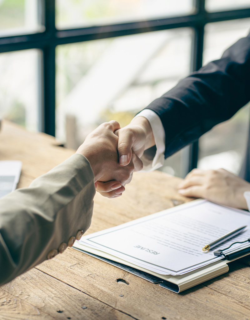 Poignée de main entre deux personnes en costume, avec un CV sur la table, symbolisant un accord d'embauche.