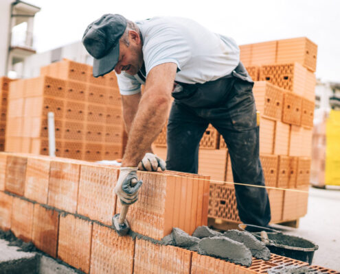 Maçon posant des briques avec précision sur un chantier, utilisant une truelle et du mortier.